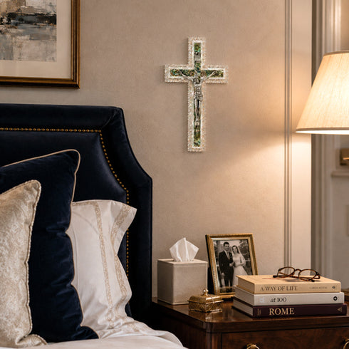 Decorative cross on a wall above a bed with pillows and a lamp.