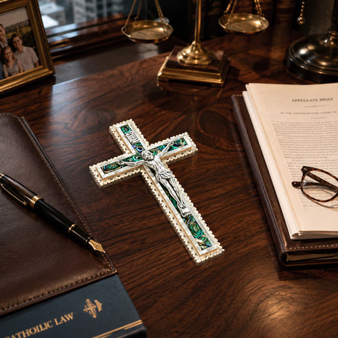 Decorative cross on a wooden desk with books, glasses, and a pen.