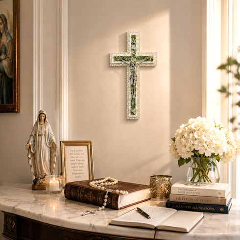Decorative setup with a cross, statue, books, and flowers on a marble surface.