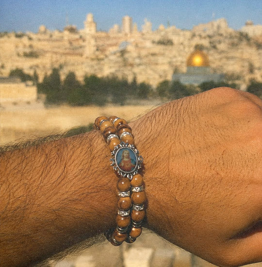 Bracelet with a portrait charm on a wrist, with a blurred cityscape in the background