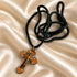 Olive wood cross pendant necklace with black braided cord, shown coiled