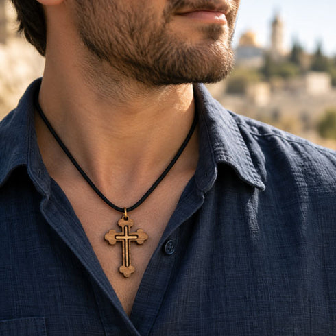 Cross pendant necklace on a man in a blue shirt, black cord and olive wood cross