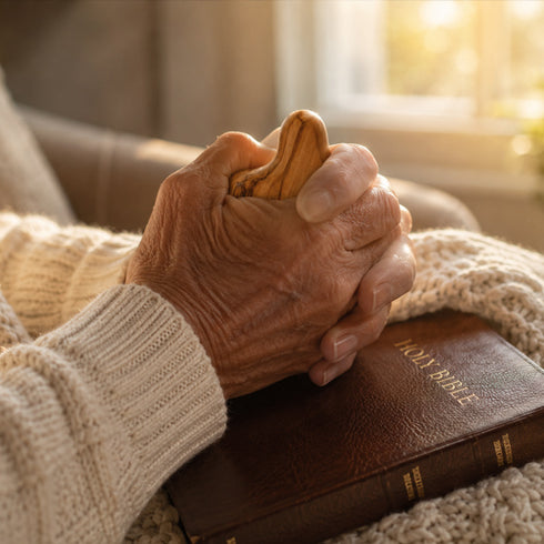 Close-up of an elderly person's hands holding a comfort cross over a Holy Bible.