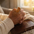 Close-up of an elderly person's hands holding a comfort cross over a Holy Bible.