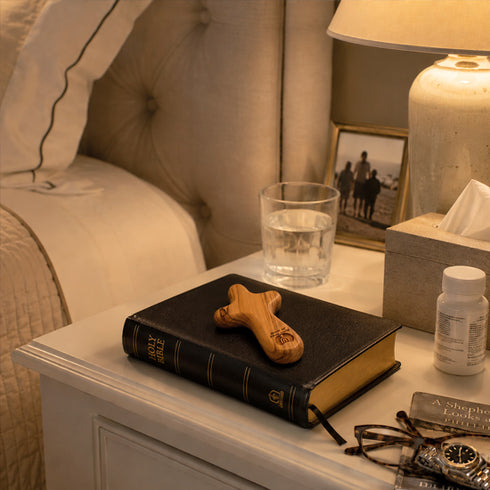 Nightstand with a Bible, comfort cross, glass of water, and other items.
