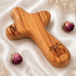 Olive wood comfort cross with the Piece of Holy Land logo, shown on white background with roses