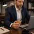 Man in a suit holding a comfort cross in front of a laptop at a desk.