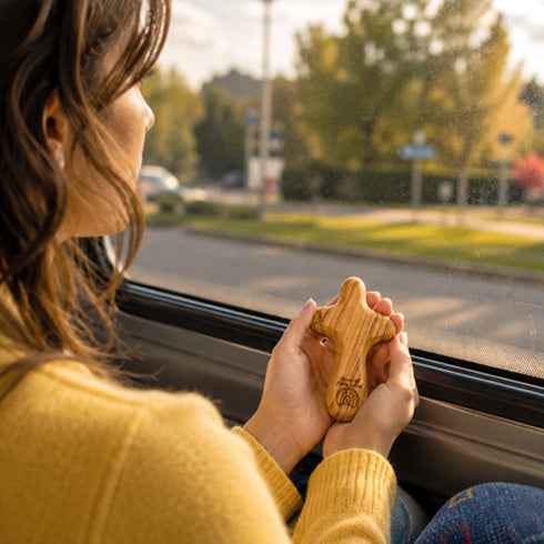 Person holding a comfort cross by a car window with a scenic road view.