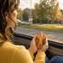 Person holding a comfort cross by a car window with a scenic road view.