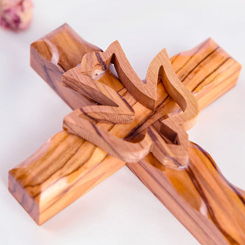 Detail image of a handcrafted olive wood cross featuring an embossed dove motif, set against a white background with a petal.