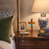 Nighstand with decorative items including a lamp, cross, and books next to a bed with patterned pillows.