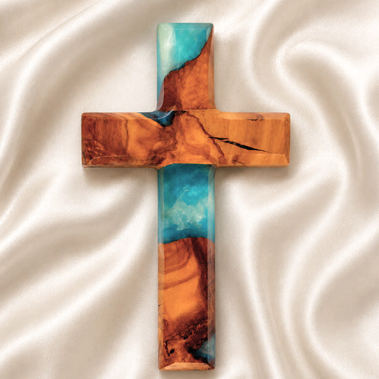 Wooden cross with blue and brown resin on a white fabric background