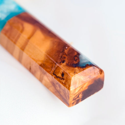 Close up image of a bottom of an handcrafted olive wood cross with blue and green epoxy, polished and displayed on a white background.