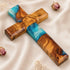 Image of a handcrafted olive wood cross with blue and green epoxy, polished and displayed on a white background.