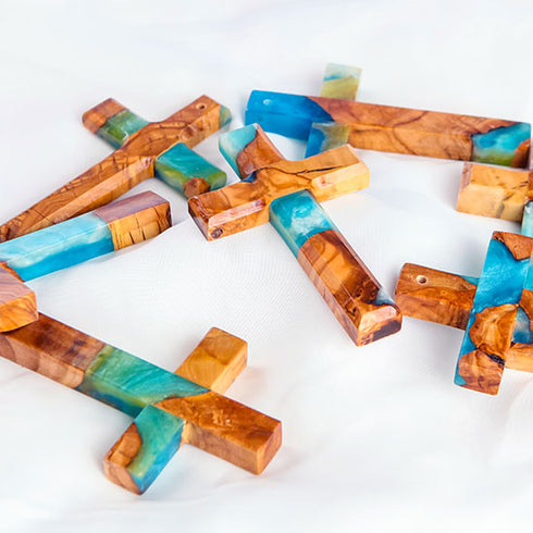 Various handcrafted olive wood crosses with blue and green epoxy, finely polished and displayed on a white background.