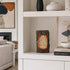 Decorative cross on a shelf in a living room setting with books and art.