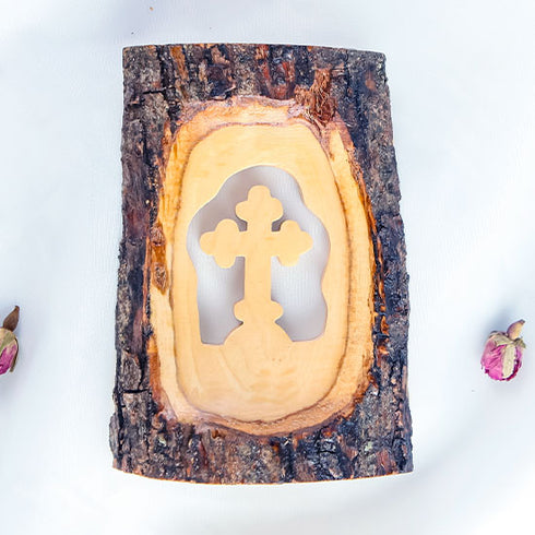 Pack shot of a standing olive wood cross handmade of natural bark, placed on a white cloth with petals.