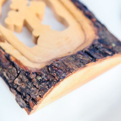Close up of a handmade olive wood cross made of natural bark, placed on a white cloth background.