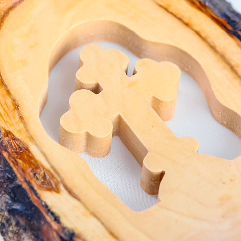 Close up of standing olive wood cross handmade of natural bark, placed on a white cloth background with petals.