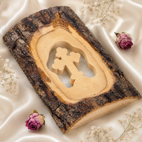 A standing olive wood cross made of natural bark, placed on a white cloth background with petals.