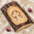 A standing olive wood cross made of natural bark, placed on a white cloth background with petals.