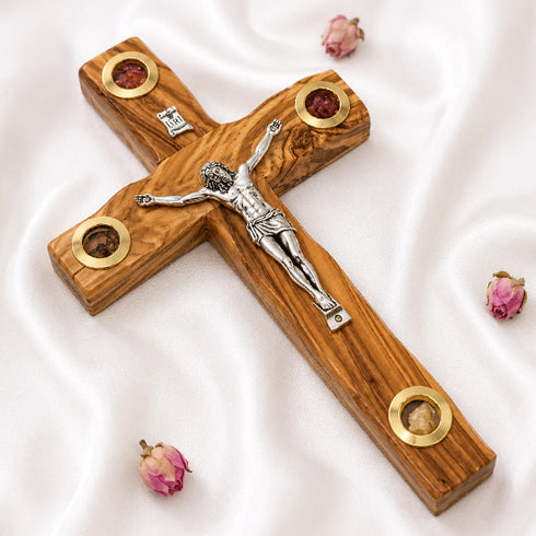 Wooden cross with a silver Jesus figure on a white background with dried flowers.