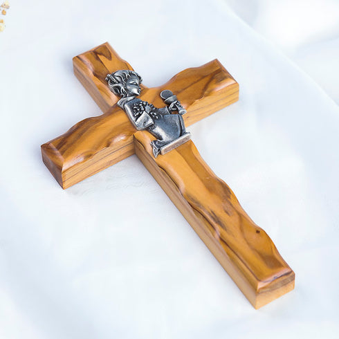 A handcrafted olive wood cross with a metal emblem of a praying girl on it.