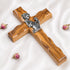 A handcrafted olive wood cross with a metal emblem of a praying girl on it.