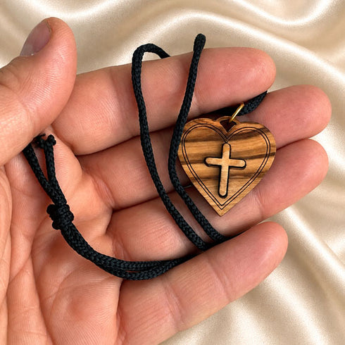 Olive wood heart pendant with cross on black cord, held in hand