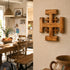 Wooden Jerusalem cross wall art on a beige wall with a kitchen in the background.