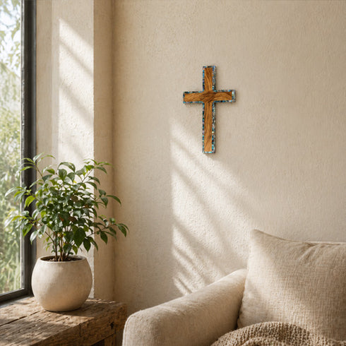 Olive wood cross on a wall next to a window and a plant