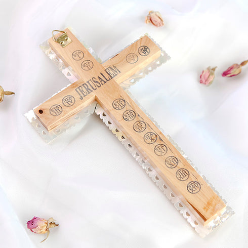 Back of a Latin-style olive wood cross with "Jerusalem" and the Stations of Cross written on it, against white background with rose petals around it.
