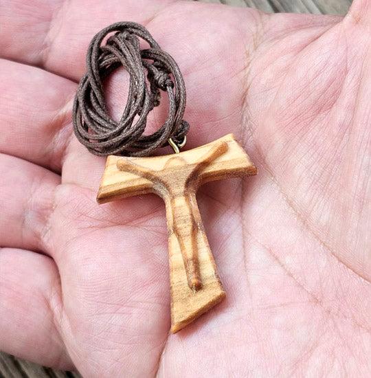 Wooden TAU cross pendant on a cord held in a hand