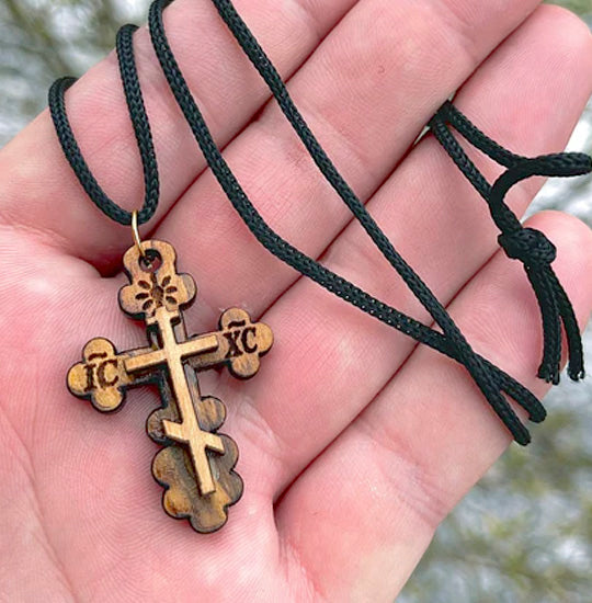 Wooden cross pendant on a black cord held in a hand with a blurred natural background