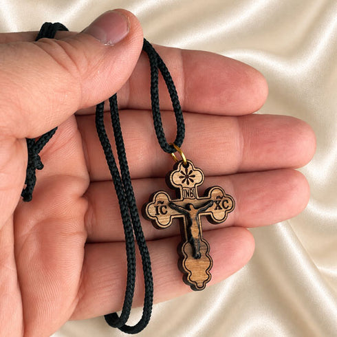 Hand holding an Orthodox cross pendant on black braided cord, gold clasp