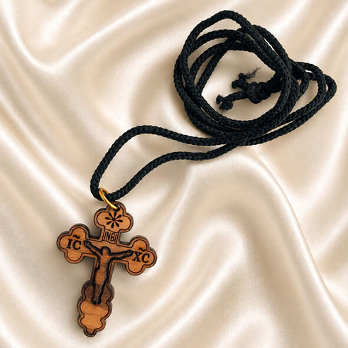 Wood Orthodox cross necklace with black braided cord, flat lay on satin