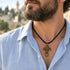 Cross pendant necklace on black cord, worn on a man in a light blue shirt