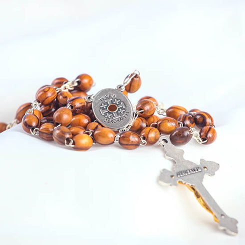 Pack-shot of a handmade olive wood rosary with Holy Soil centrepiece featuring a an iron cross with word "Jerusalem" written on it.