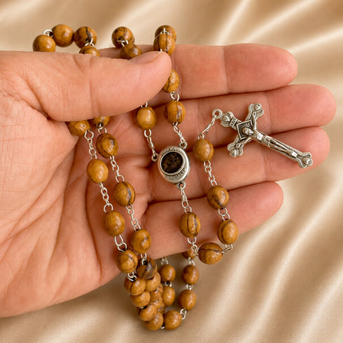 Handheld olive wood rosry with Holy Soil centrepiece medal and asilver crucifix, on a beige background.