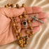 Handheld olive wood rosry with Holy Soil centrepiece medal and asilver crucifix, on a beige background.