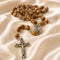 Olive wood rosary with Holy Water centerpiece on a creamy color cloth.