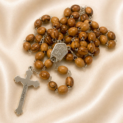 Olive wood rosary with Jerusalem cross on the back of the centerpiece on a creamy cloth.