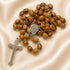 Olive wood rosary with Jerusalem cross on the back of the centerpiece on a creamy cloth.