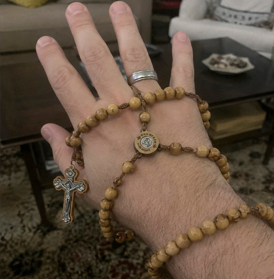 Hand wearing a wooden rosary with a cross charm in a casual indoor setting