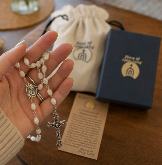 Hand holding a rosary with a branded box and drawstring bag in the background