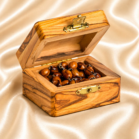 An open wooden box brass clasp, filled with brown wooden beads, set against a beige satin fabric background.