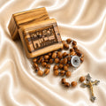 A wooden rosary , a silver-tone centerpiece, and crucifix, on draped satin next to a engraved wooden box labeled Jerusalem.