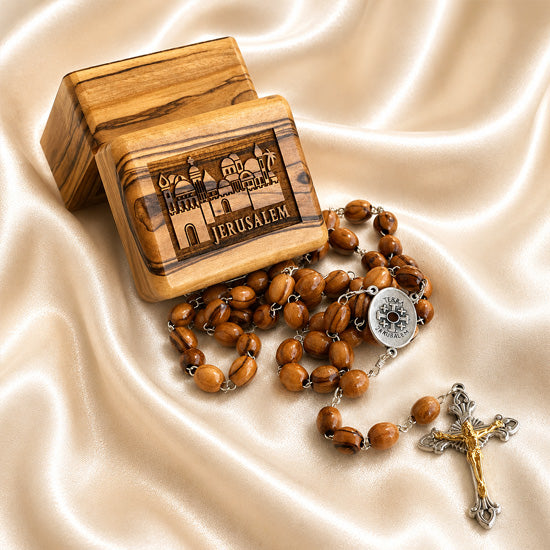 A wooden rosary , a silver-tone centerpiece, and crucifix, on draped satin next to a engraved wooden box labeled Jerusalem.