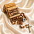 A wooden rosary , a silver-tone centerpiece, and crucifix, on draped satin next to a engraved wooden box labeled Jerusalem.