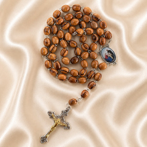 A wooden beads rosary, a medallion, and a crucifix with gold and silver details, arranged on a beige fabric background.